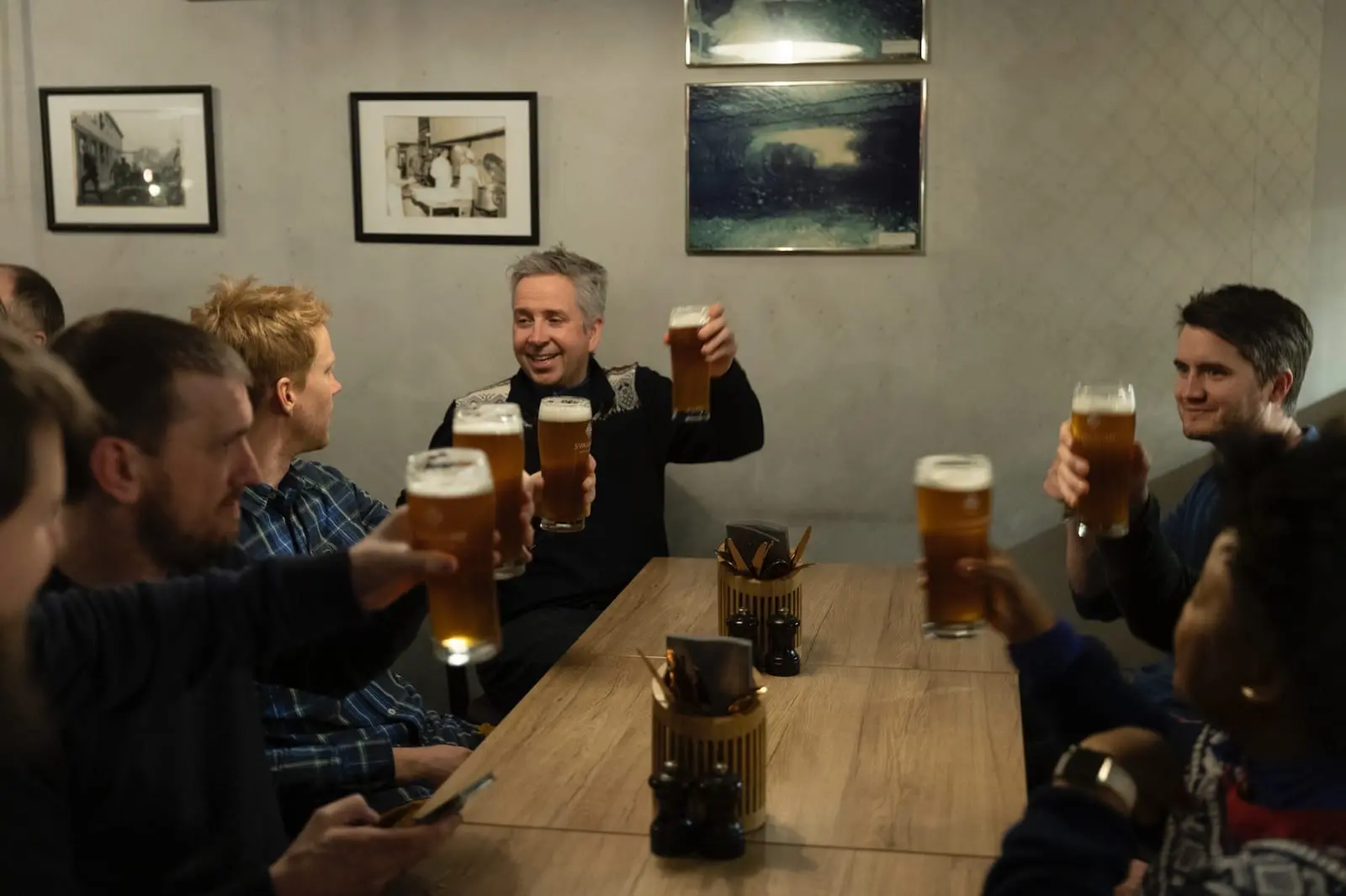Kolleger rundt et bord på en bar løfter ølglassene til skål
