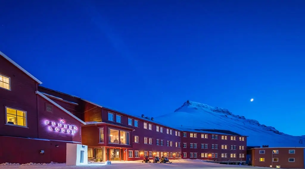 Funken Lodge, en rød hotellbygning i kveldslys med et snødekt fjell og månen bak